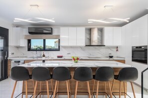 A modern kitchen with a large island, black bar stools, and a view of the outdoors. - Rhodes Villa Billys in Sgourou (Rhodes)
