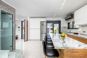 A modern kitchen with a marble countertop, stainless steel appliances, and a dining area with black chairs. - Rhodes Villa Billys in Sgourou (Rhodes)