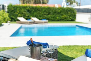 A poolside setting with lounge chairs, a pool, and a table with a bottle and glasses. - Rhodes Villa Billys in Sgourou (Rhodes)