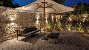 Ein Sitzbereich im Freien mit einer Steinmauer, einem Holztisch, einer Couch und einem großen Sonnenschirm.