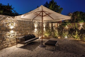 Ein Sitzbereich im Freien mit einer Steinmauer, einem weißen Sonnenschirm und einem Holztisch.