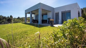 A modern house with a covered patio, a well-maintained lawn, and a view of the surrounding landscape. - High View Villa in Afantou (Rhodes)