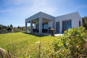 A modern house with a covered patio, a well-maintained lawn, and a view of the surrounding landscape. - High View Villa in Afantou (Rhodes)