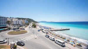 Eine Küstenstraße mit einem Strand auf der rechten Seite, gesäumt von Sonnenschirmen und Liegestühlen.