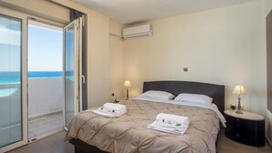 Ein Hotelzimmer mit Bett, zwei Nachttischlampen, einer Klimaanlage und Blick auf den Ozean durch eine Schiebetür.