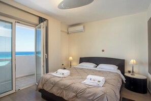 A hotel room with a bed, two bedside lamps, an air conditioning unit, and a view of the ocean through a sliding glass door. - Molos Seaside Apartment in Rhodes Town (Rhodes)