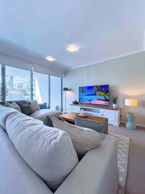 A modern living room with a large window, a flat-screen TV, and a sofa. - The New Paradise Retreat (Surfers Paradise)