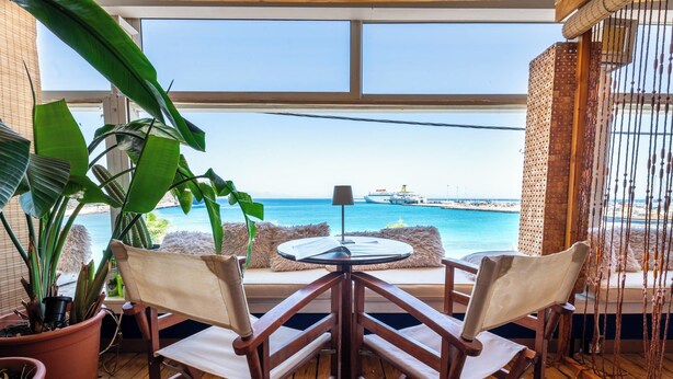 A wooden deck with a table and chairs, potted plants, and a view of the sea and a ship. - La Terrazza Sul Mare in Rhodes Town (Rhodes)