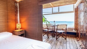 A room with a bed, a nightstand with a lamp, a wooden floor, and a view of the ocean. - La Terrazza Sul Mare in Rhodes Town (Rhodes)