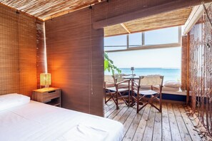 A room with a bed, a nightstand with a lamp, a wooden floor, and a view of the ocean. - La Terrazza Sul Mare in Rhodes Town (Rhodes)