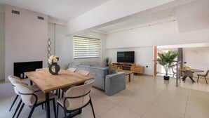 Una sala de estar moderna con una mesa de comedor de madera, sofás grises, un televisor de pantalla plana y una planta en maceta.