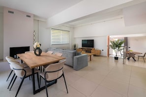 Ein modernes Wohnzimmer mit einem Holzesstisch, grauen Sofas, einem Flachbildfernseher und einer Topfpflanze.