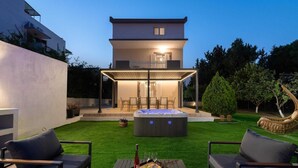 Una casa moderna con jacuzzi, mobiliario exterior y césped cuidado.