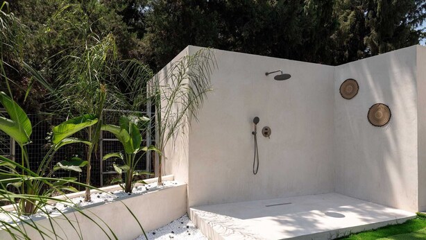 Un área de ducha exterior moderna con un banco integrado, rodeada de follaje y un muro de hormigón.