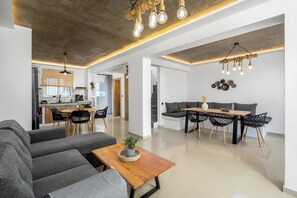 Ein modernes Wohnzimmer mit grauem Sofa, Couchtisch aus Holz und einem Essbereich mit Holztisch und schwarzen Stühlen.