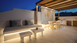 An outdoor living area with a sofa, dining table, and chairs, a kitchen area, and a view of the cityscape. - ArmoniKon Pool Villas - Villa 2 (Rhodes)