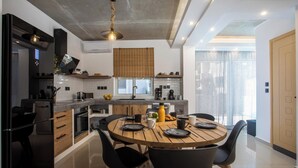 A modern kitchen with a central island, black chairs, and a round wooden table. - ArmoniKon Pool Villas - Villa 2 (Rhodes)