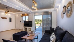 A modern living room with a sofa, a coffee table, and a television. - ArmoniKon Pool Villas - Villa 2 (Rhodes)