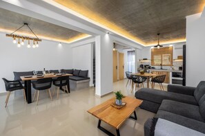 A modern living room with a sofa, dining table, and chairs. There is a kitchen area with a dining table and chairs. - ArmoniKon Pool Villas - Villa 3 (Rhodes)