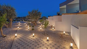 A modern outdoor area with a paved walkway, trees, and outdoor lighting. - Tota Suites - Suite 1 (Rhodes)