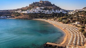 A coastal town with a castle on a hill, a beach with umbrellas, and white buildings. - Retreat Apartment in Rhodes Town (Rhodes)