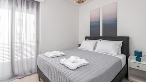 A neatly made bed with white linens, a grey headboard, and a bedside table with a blue lamp. - Retreat Apartment in Rhodes Town (Rhodes)