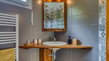Un baño con tocador de madera, un lavabo blanco, un espejo con marco de madera y azulejos estampados.