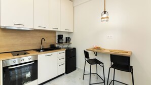 Una cocina moderna con armarios blancos, un refrigerador negro, una cafetera y dos taburetes negros.
