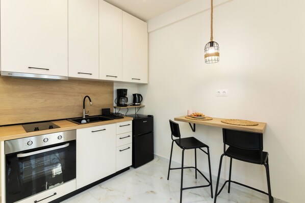 A modern kitchen with white cabinets, a black refrigerator, a coffee maker, and two black bar stools.