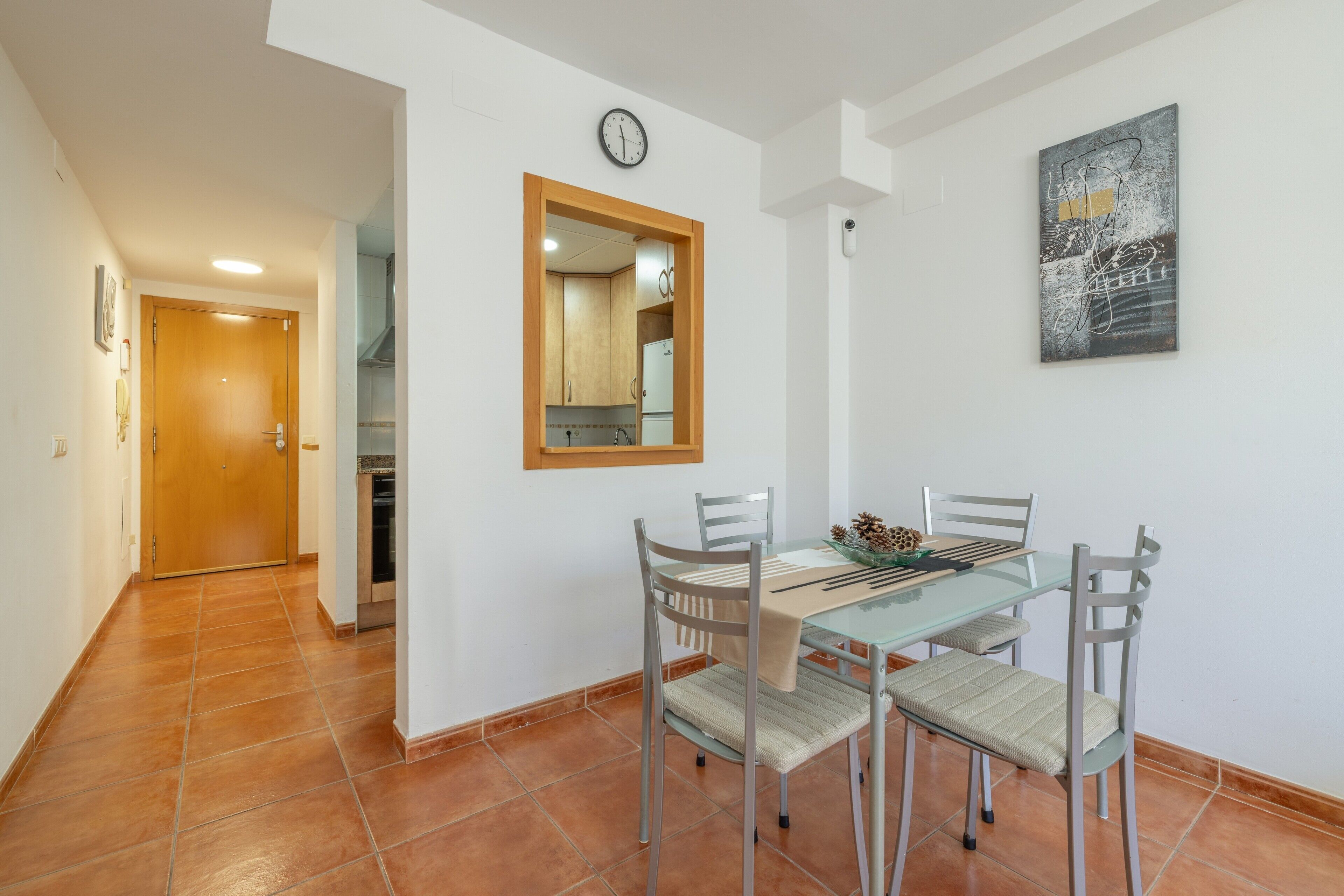 Un coin repas avec une table en verre, des chaises en métal, un miroir à cadre en bois et une horloge au mur.