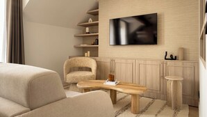Un salon moderne doté d’un téléviseur à écran plat, d’un canapé, d’un fauteuil, d’une table basse en bois et d’étagères intégrées.