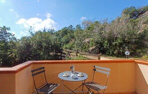 Ein Balkon mit zwei Metallstühlen und einem kleinen runden Tisch mit Blick auf einen bewaldeten Hügel.