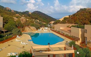 Ein Pool, umgeben von Liegestühlen, mit einer Bergkulisse im Hintergrund.