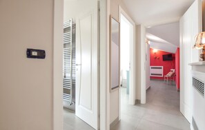 Un couloir avec une porte blanche, un porte-serviettes en métal et un mur rouge orné d’un téléviseur.