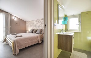 Une chambre à coucher avec un lit, une table de chevet et une salle de bain équipée d’un lavabo et d’un miroir.