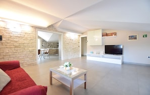 Una sala de estar moderna con una mesa de centro de vidrio, un sofá rojo, un televisor y un área de cocina visible a través de una puerta abierta.