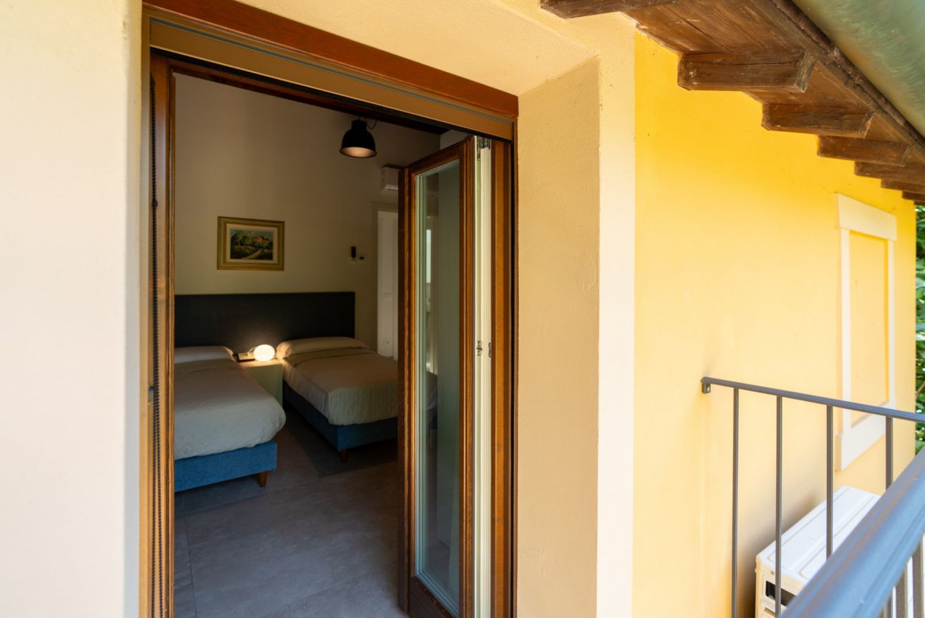 Une chambre avec deux lits, une table de chevet, une lampe et une porte donnant sur une autre pièce.
