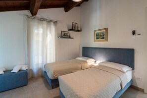Une chambre avec deux lits, une tête de lit bleue, une table de chevet, une fenêtre avec des rideaux et des étagères murales décorées de tableaux.