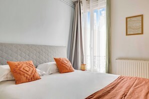 A bed with a quilted headboard, two pillows, a bedside lamp, and a window with curtains. - Charming Apartment 2BR/4P - Saint-Denis (Saint-Denis)