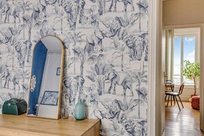 A room with a patterned wallpaper, a mirror, a small table with a vase, and a view of a balcony with a plant. - Charming Apartment 2BR/4P - Saint-Denis (Saint-Denis)