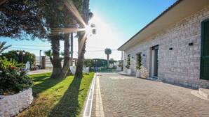 Un cortile lastricato con muri in pietra, una zona verdeggiante e un edificio con una porta e finestre.