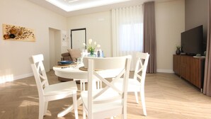 Un soggiorno moderno con zona pranzo, televisore a schermo piatto e ampia finestra con tende.
