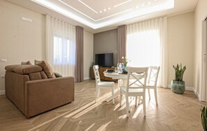 Ein Wohnzimmer mit Sofa, Esstisch, Stühlen, einem Fernseher und einer Topfpflanze.