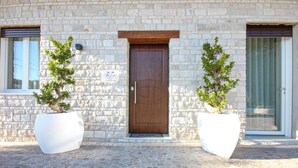 Un edificio in pietra con una porta di legno, due piante in vaso e un ingresso lastricato con pietre.