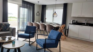Un salon moderne comprenant un canapé, deux fauteuils bleus, une petite table ronde et un coin repas avec une table et des chaises.