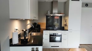 Une cuisine moderne avec des meubles blancs, un évier en acier inoxydable, une bouilloire et un four encastré.