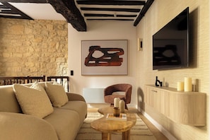 A cozy living room with a stone wall, a wooden ceiling, a sofa, a chair, a coffee table, and a mounted TV. - Premium Souplex a/c 1BR/4P – Saint-Germain (Paris)