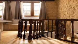 Una habitació amb una escala de fusta, parets de pedra i una finestra amb cortines.