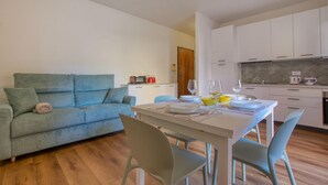 A modern living room with a sofa, dining table, and chairs. A kitchen with white cabinets and a microwave is visible in the background. - 1 bedroom awesome apartment in Recco (Recco)