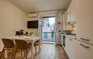 A compact kitchen with white cabinets, a dining table with chairs, and a view through an open door to a balcony. - Lovely apartment in Recco with WiFi (Recco)